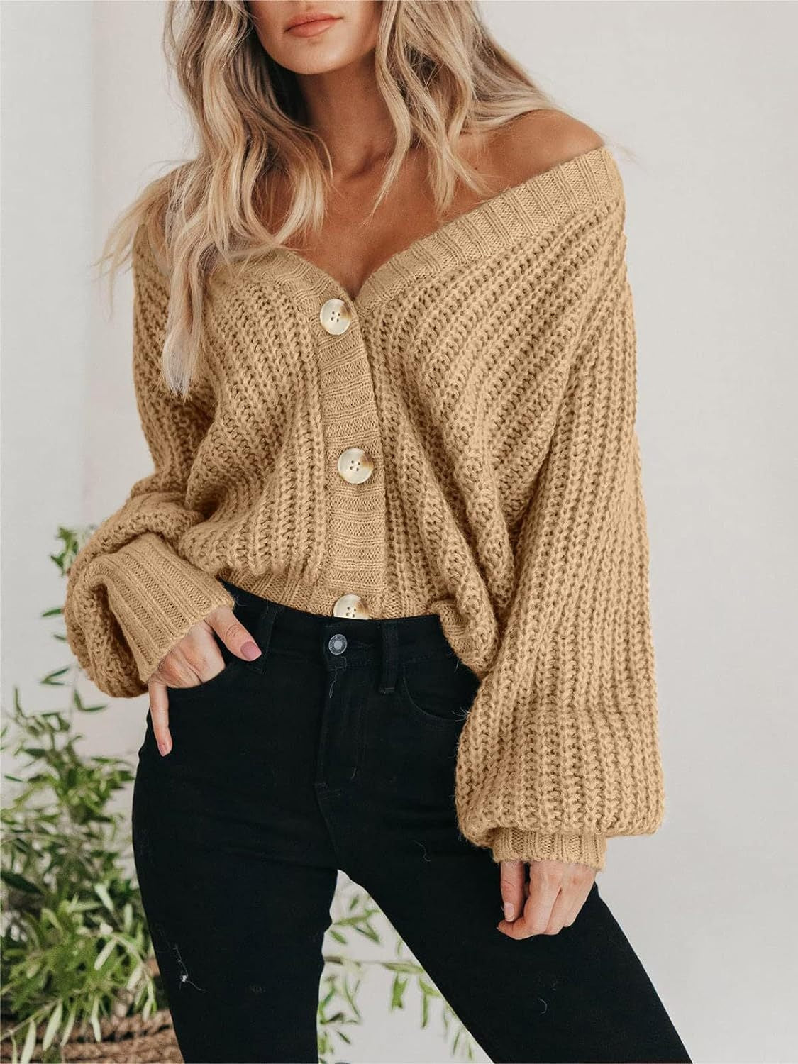 Woman wearing oversized chunky knit buttoned cardigan in tan over black jeans styled for Fall's Must-Have Sweaters guide