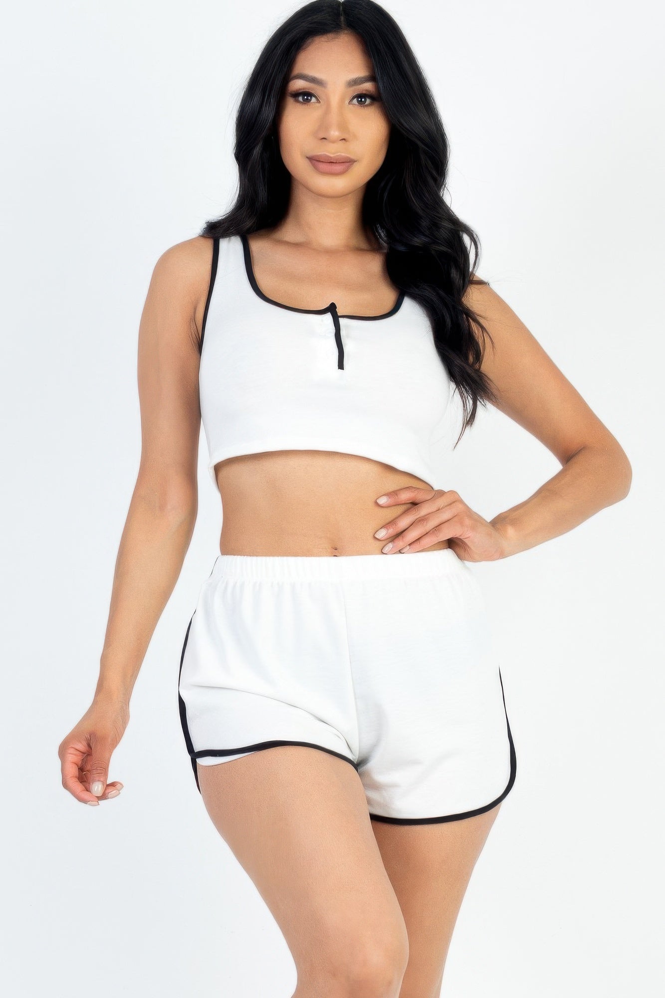 A female model wearing a white sleeveless tank top with button front and contrast trim, paired with matching shorts. The model is standing against a plain background.