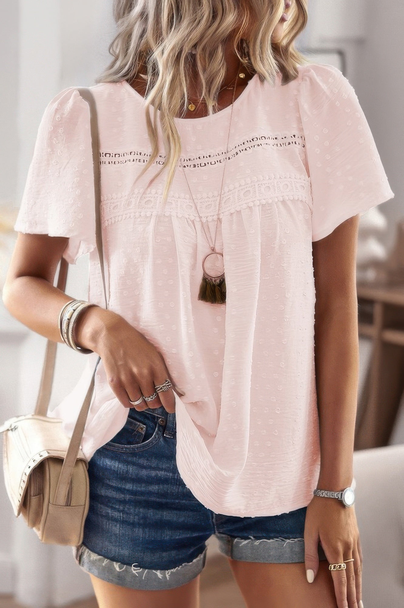 Woman wearing a plus size solid short sleeve top in light pink with lace yoke and textured dots paired with denim shorts
