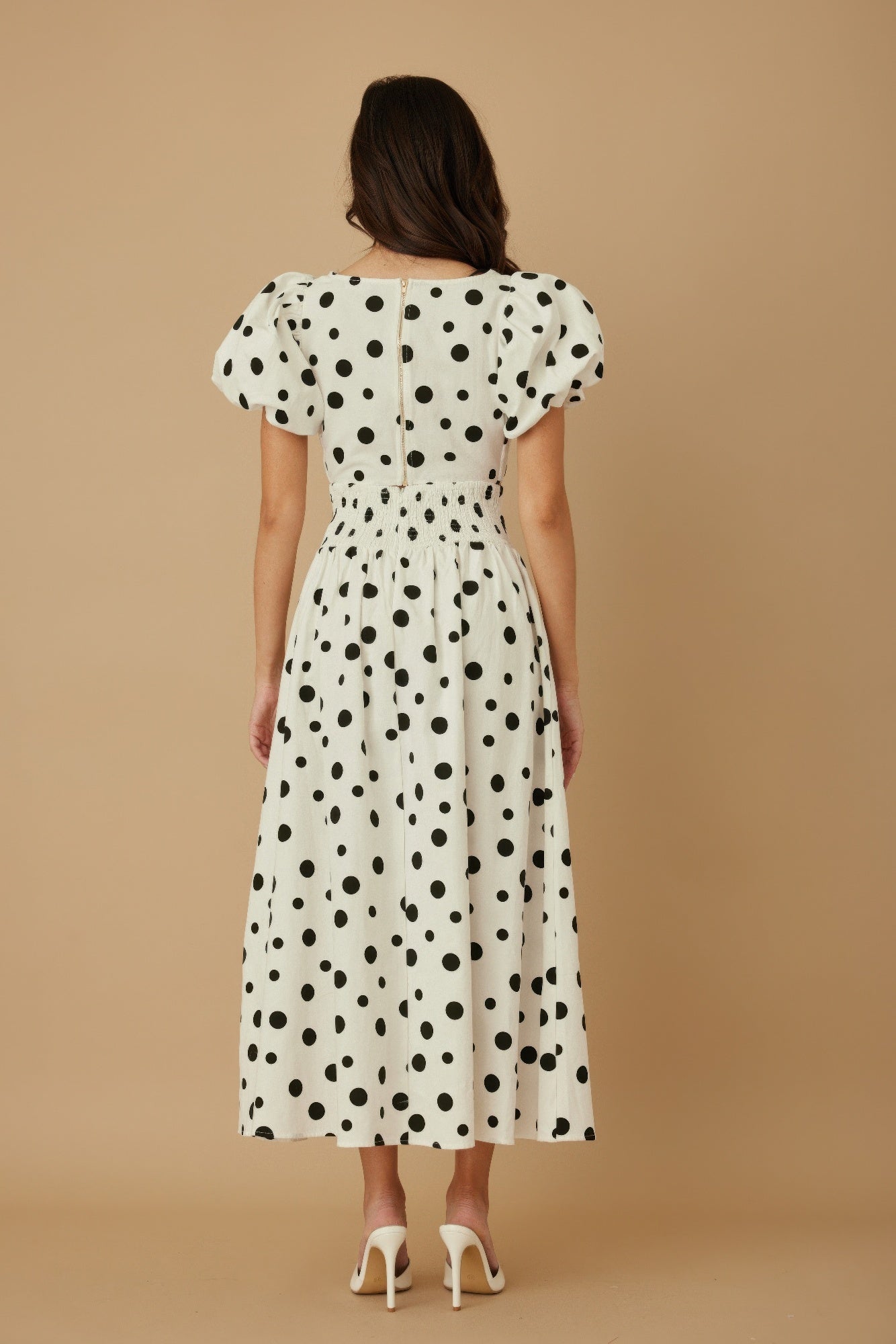 Back view of model in CCWHOLESALECLOTHING polka dot two piece set white with black dots puff sleeves smocked waist midi skirt