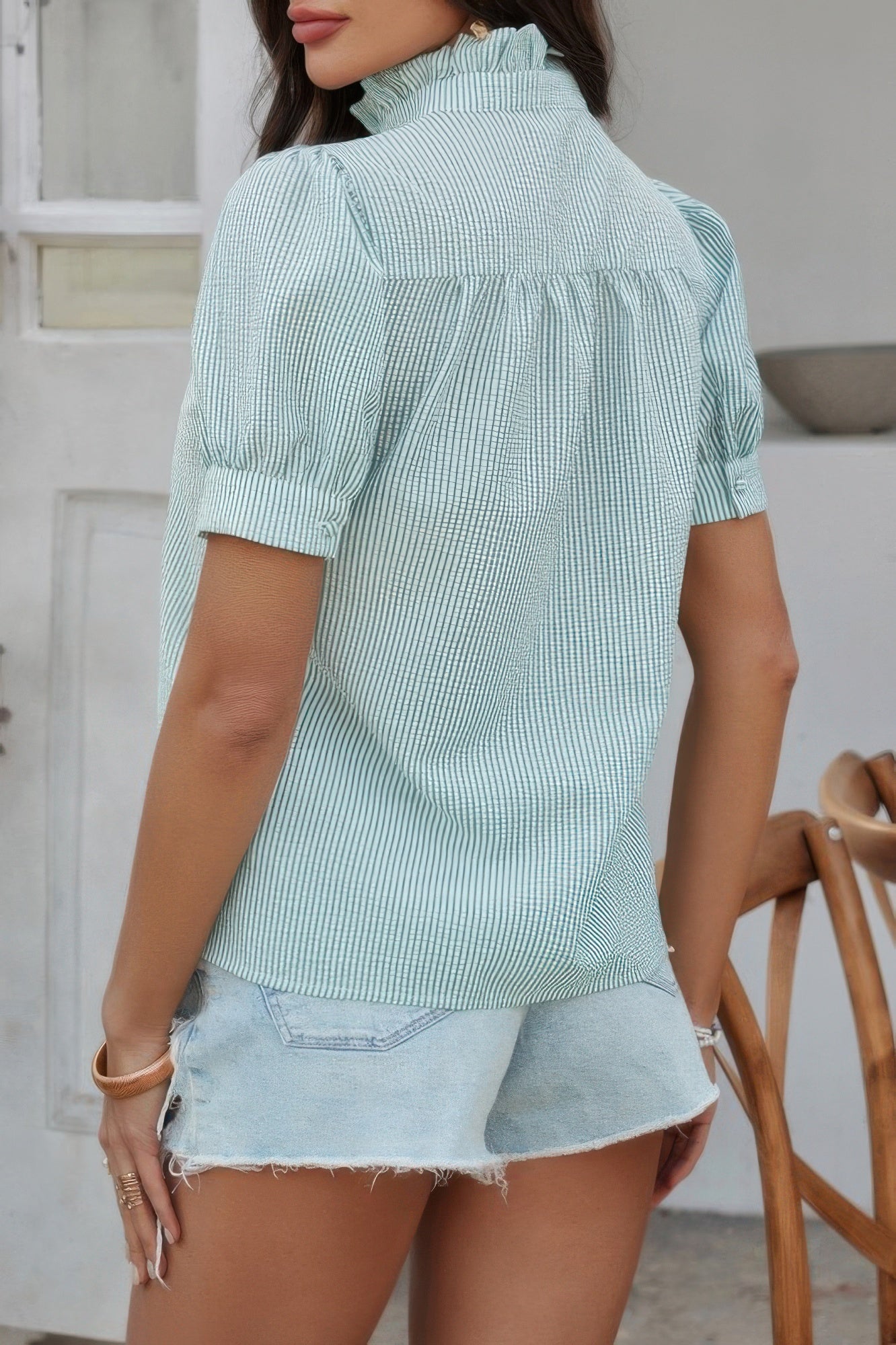 Back view of woman wearing stripe button down ruffle shirt with ruffled collar and cuffed puff sleeves