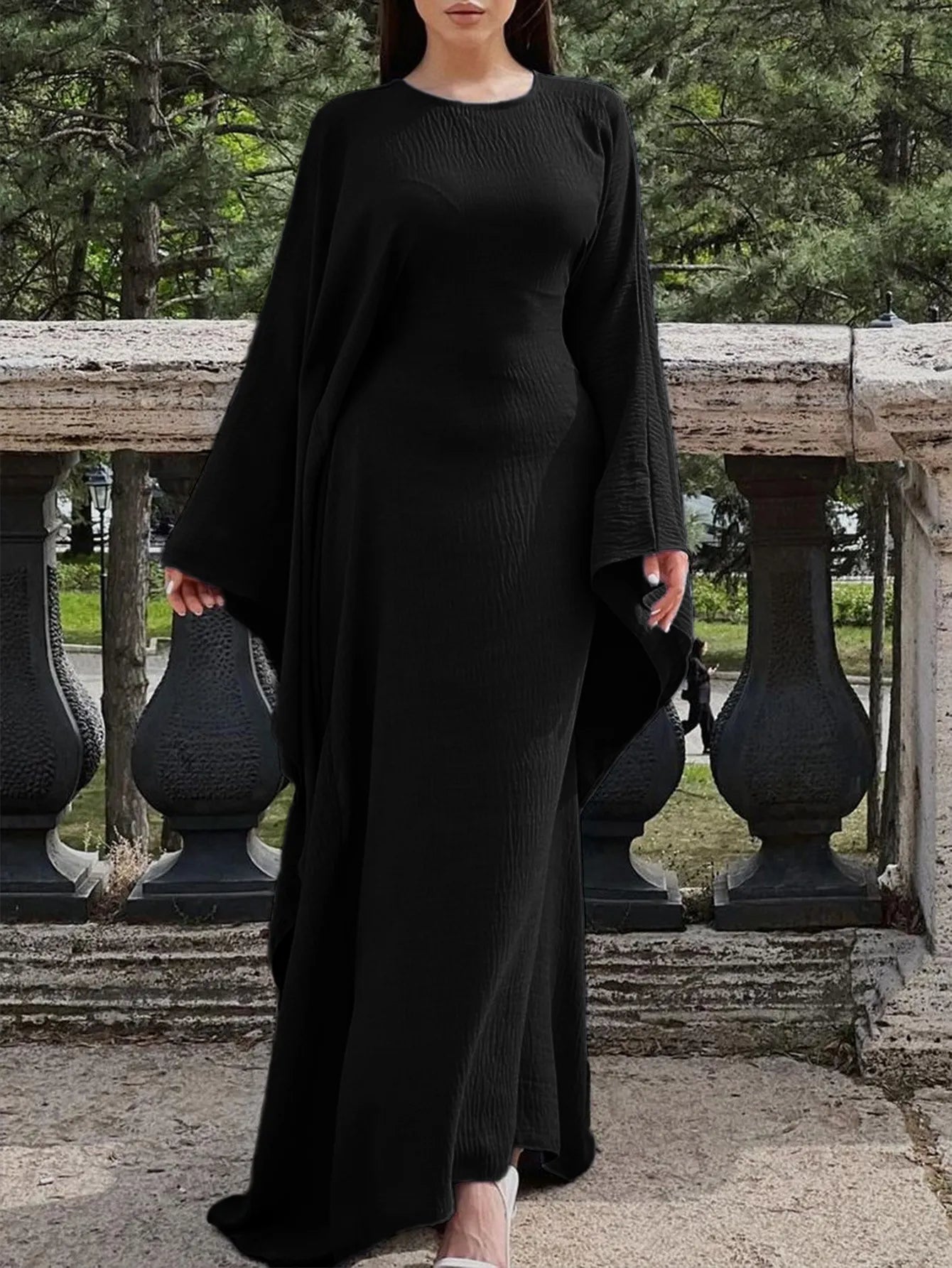 Trendsi black bohemian maxi dress with cape sleeves worn by model with round neck and flowing silhouette outdoors