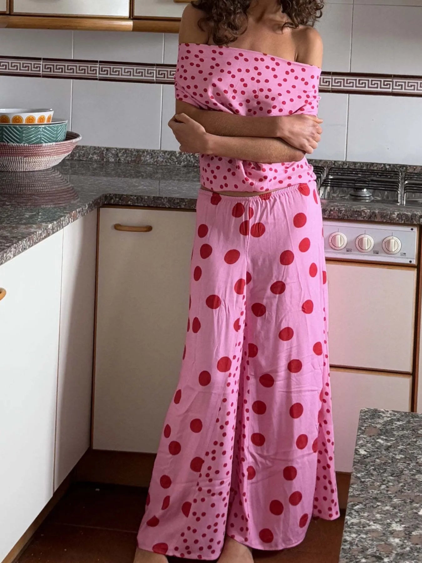 Trendsi pink polka dot off shoulder Top and Maxi Skirt Set modeled in kitchen with folded arms