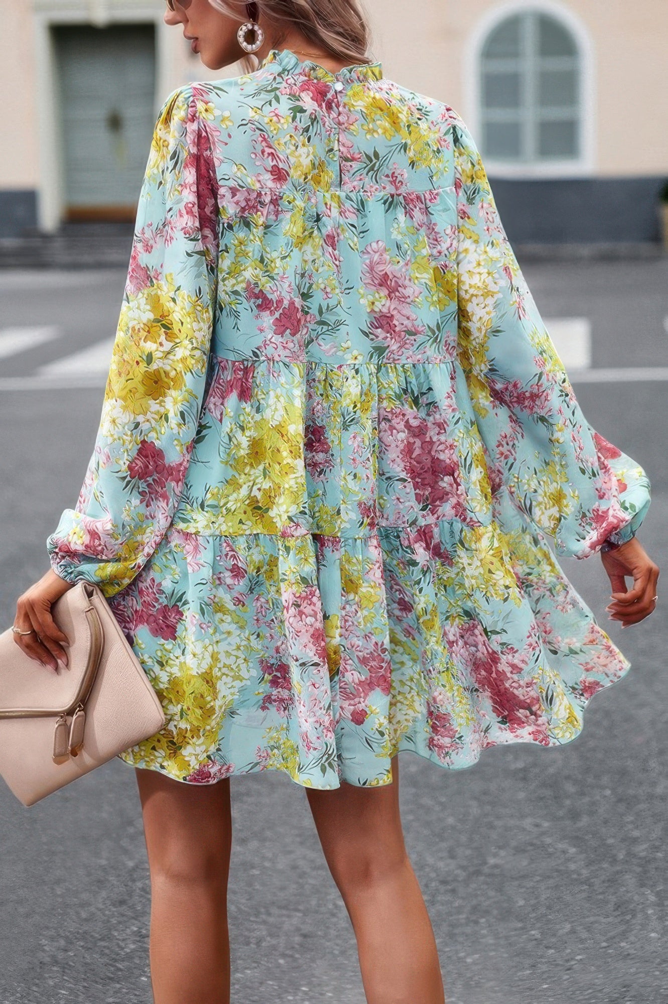 Back view of woman wearing a pastel blue floral print smock dress with long sleeves and tiered skirt