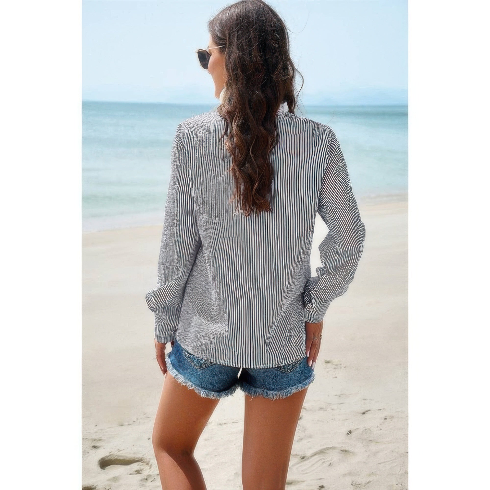 Woman on beach wearing striped long sleeve Button Front Shirt with denim cutoff shorts back view