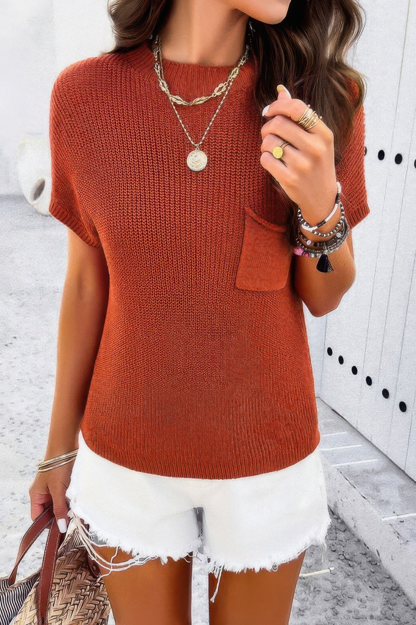 Woman wearing rust ribbed knit loose top with chest pocket white frayed denim shorts and layered jewelry