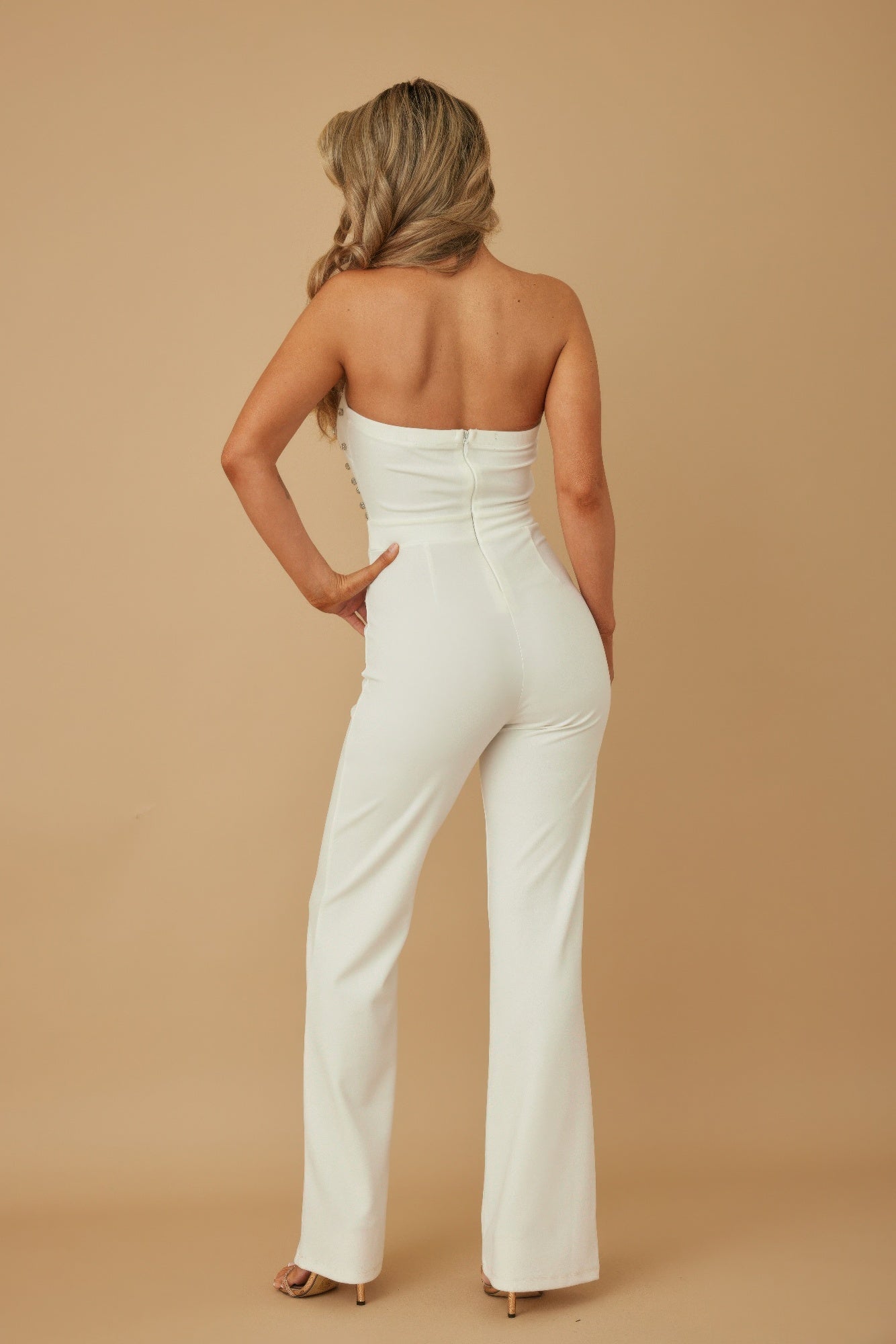 Model back view wearing white rhinestone jumpsuit for women strapless fitted bodice zip back flared leg