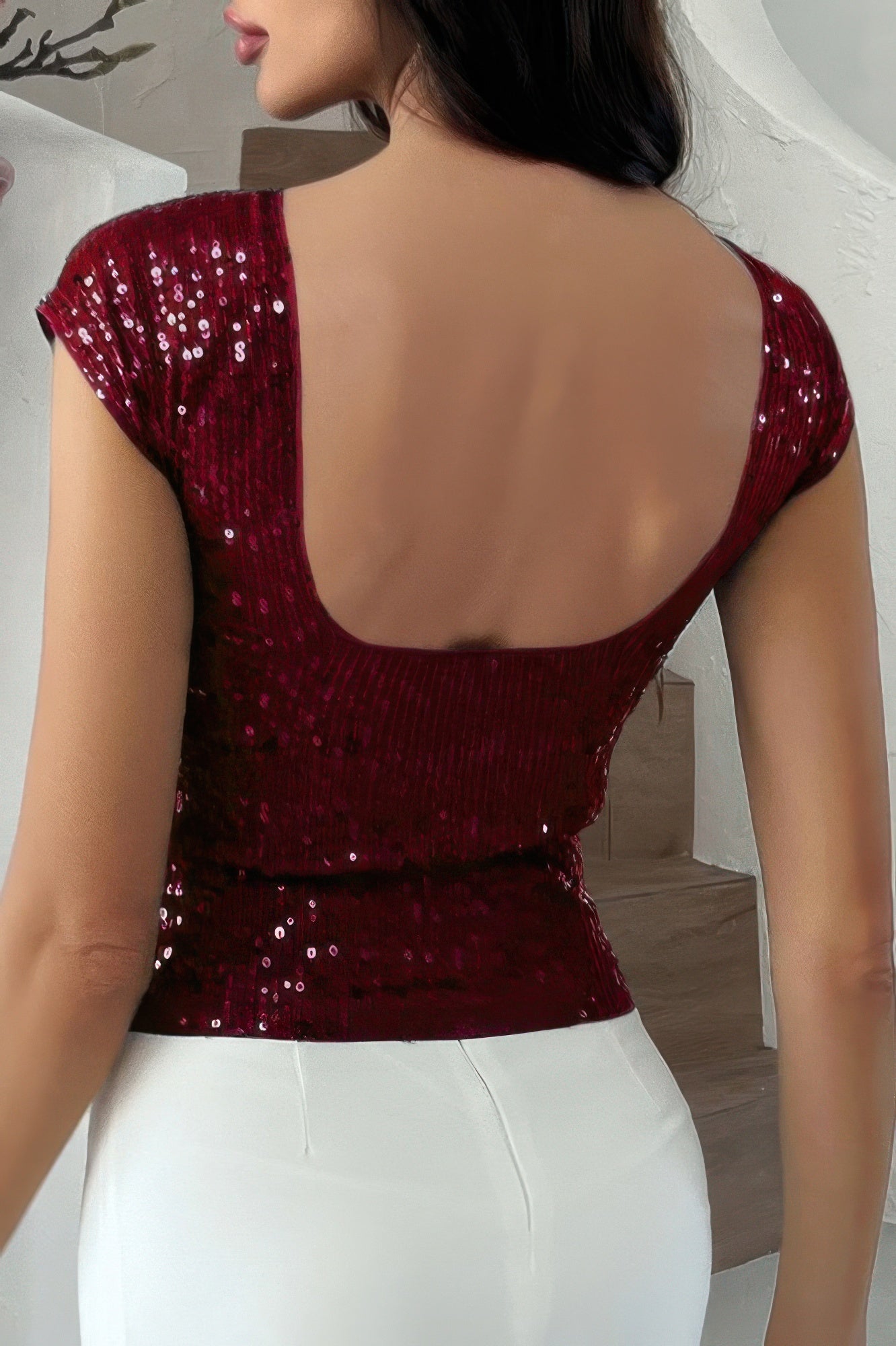 Back view of woman wearing burgundy sequin crop top with scoop back and cap sleeves paired with white pants