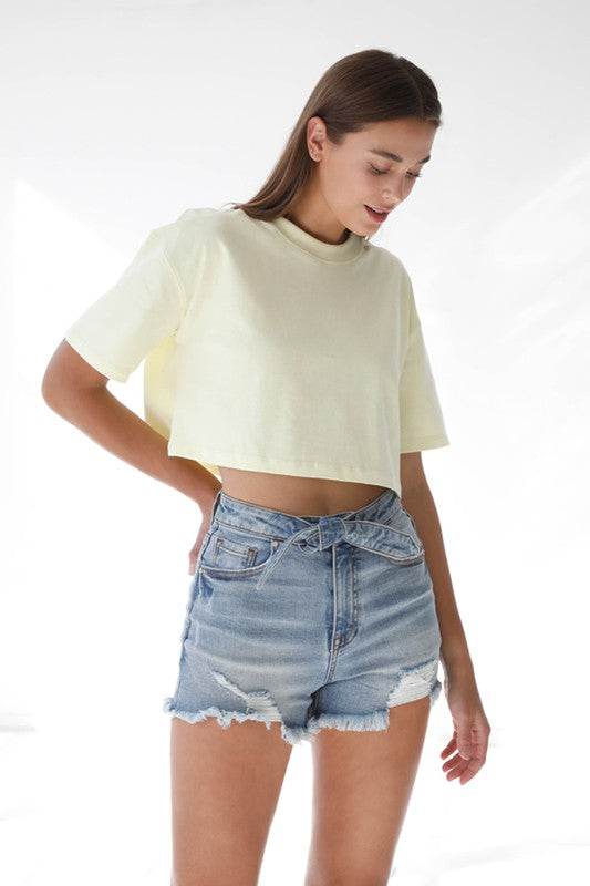 Model wearing High Waisted Denim Shorts with a relaxed fit and frayed hem, styled with a cropped top