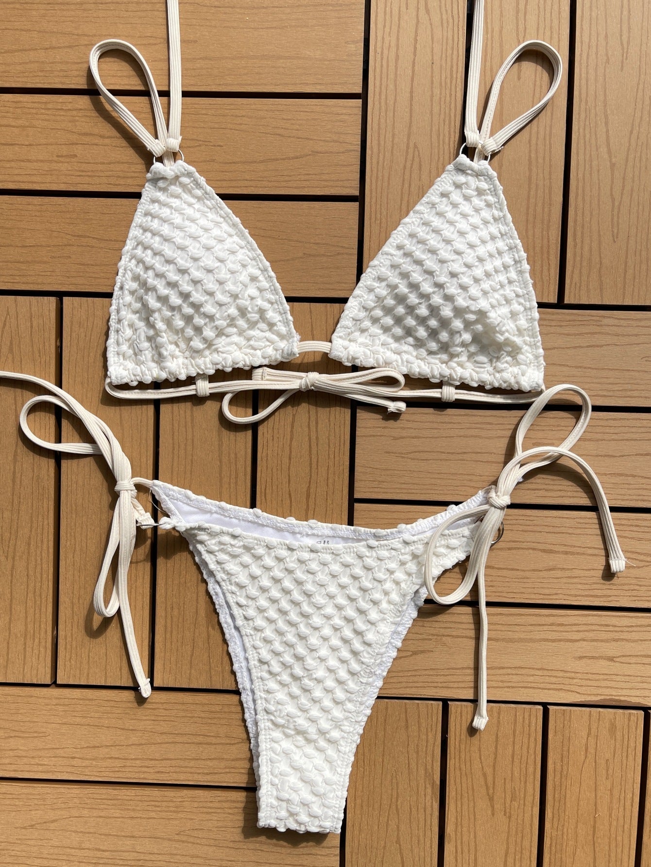 White knit textured bikini summer swimwear with adjustable straps laid flat on wooden surface