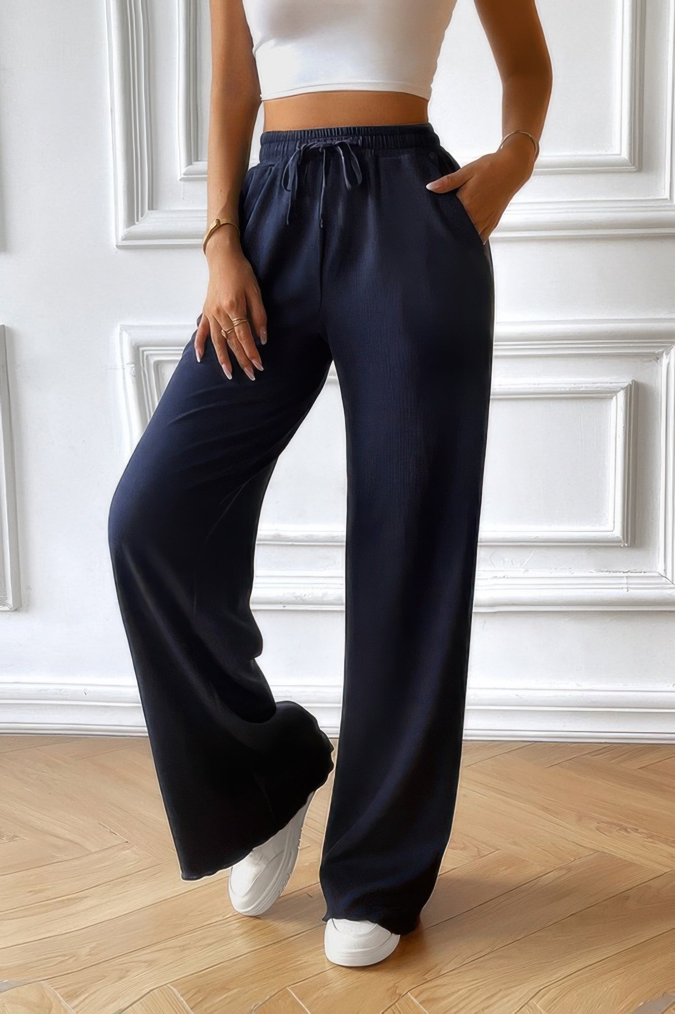Woman modeling women's elastic waist straight pants in navy with drawstring pockets paired with white crop top and sneakers