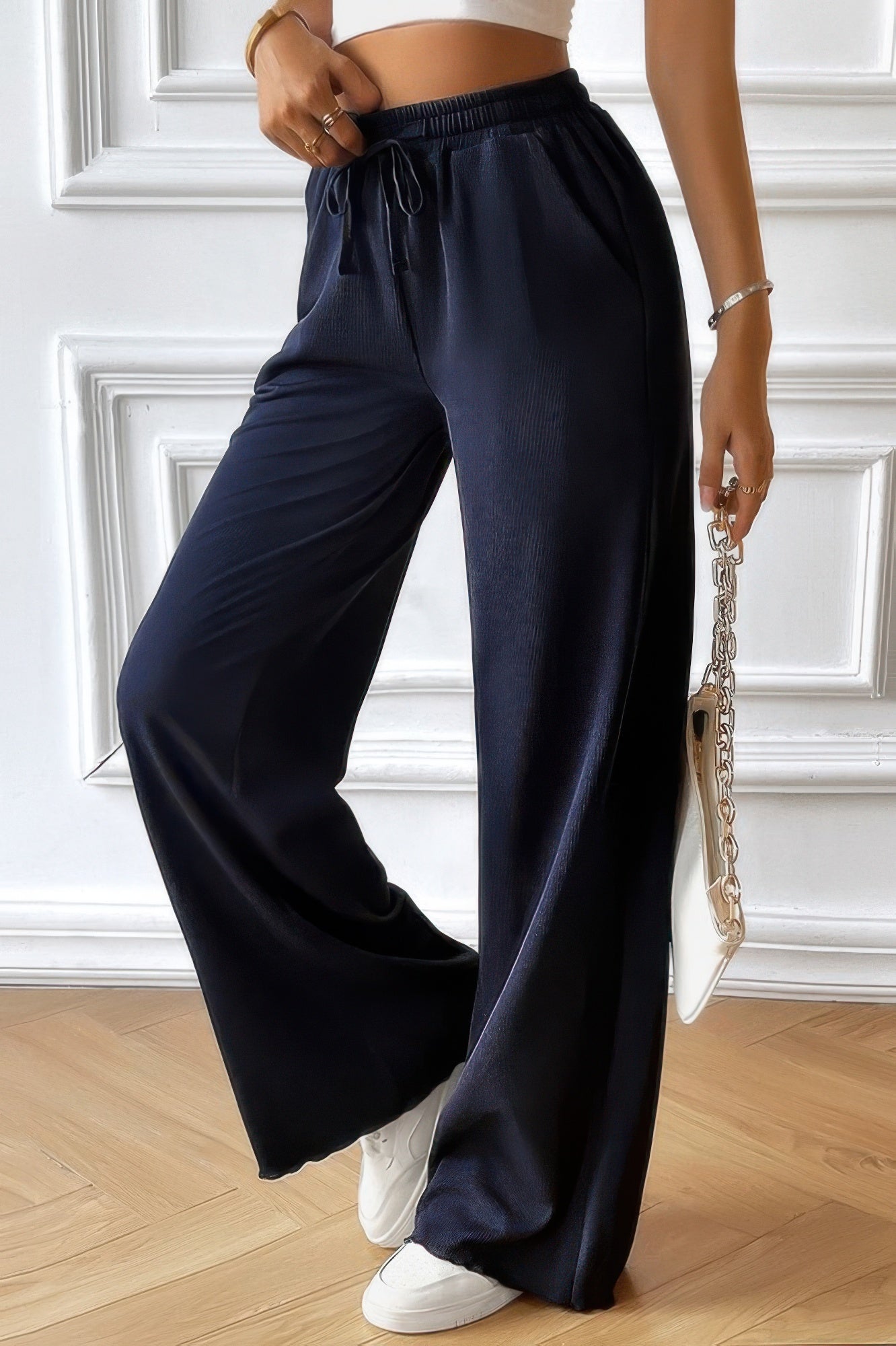 Model wearing navy women's elastic waist straight pants with drawstring, white sneakers and chain strap bag