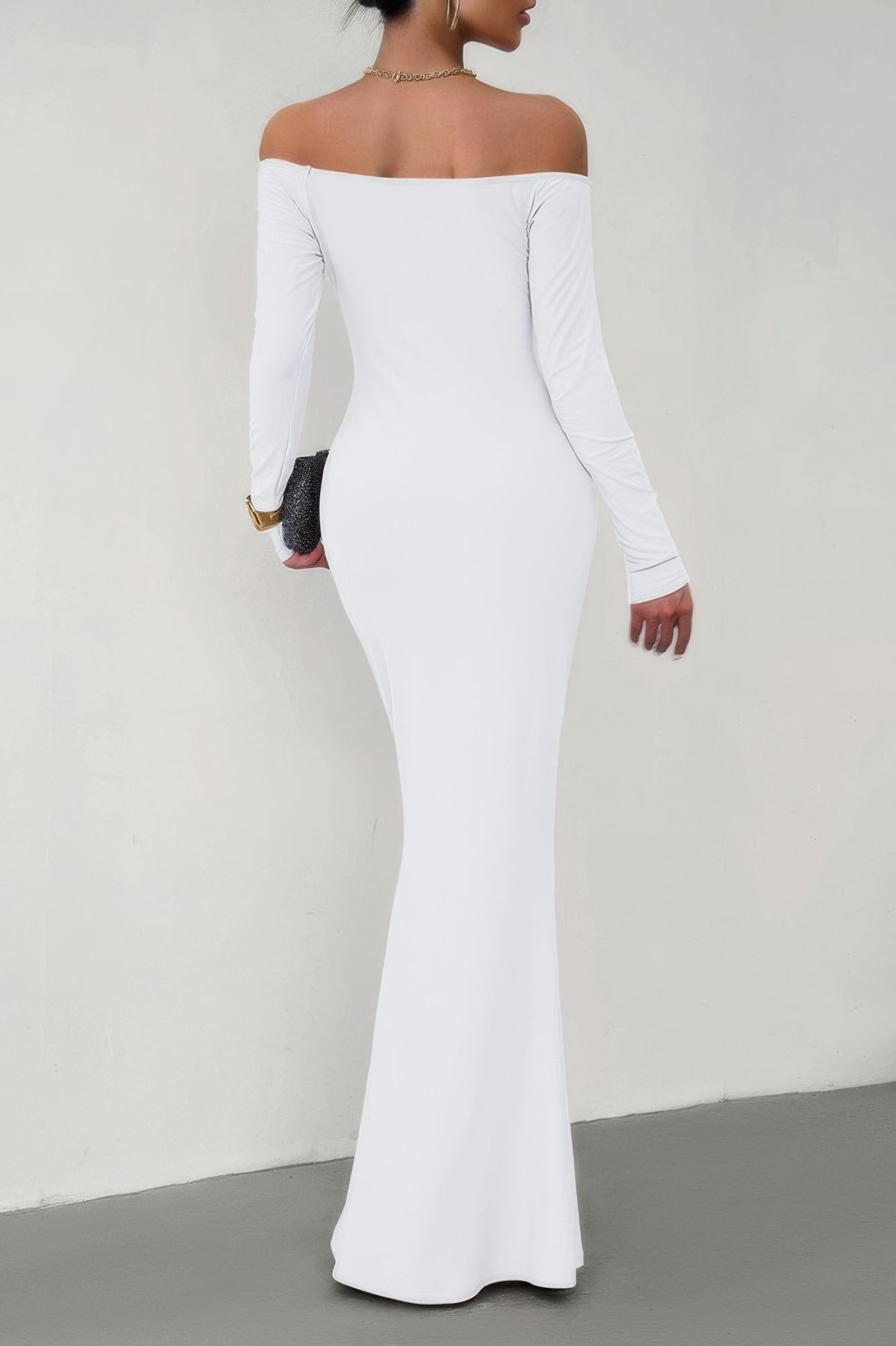 Back view of model wearing white long sleeve off shoulder bodycon dress with floor length fit clutch and gold jewelry