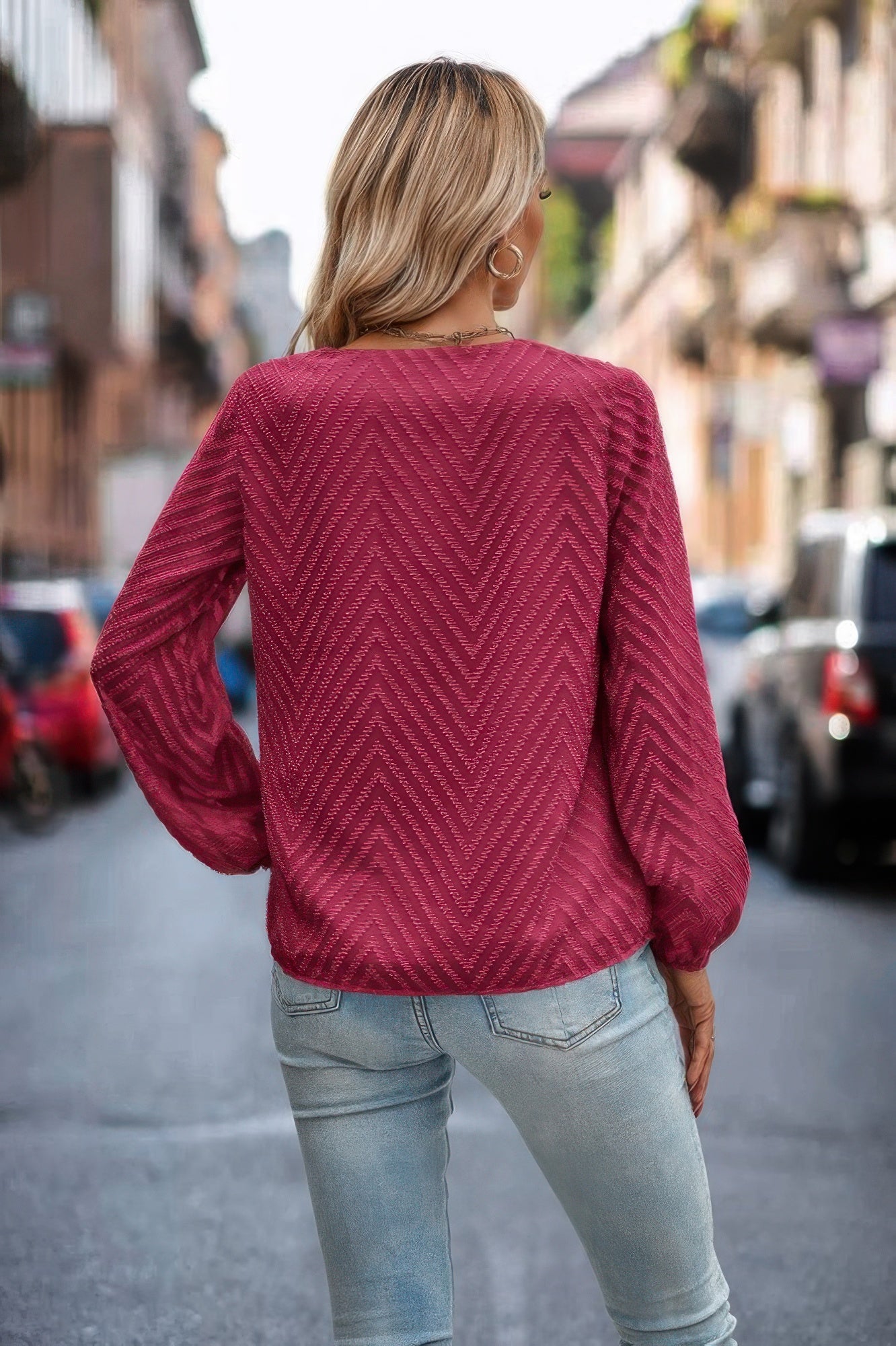 Woman wearing magenta chevron knit Long Sleeve Loose Top with balloon sleeves paired with light wash jeans on city street