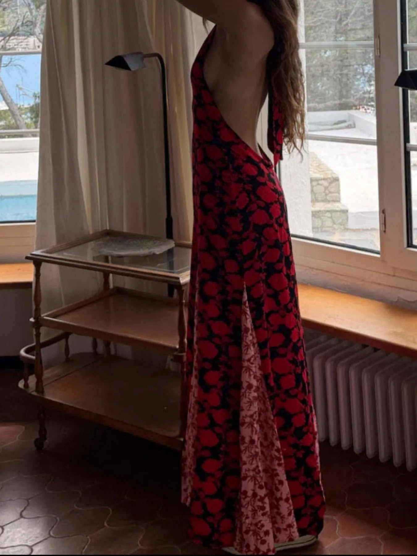 Trendsi Polka Dot Maxi Dress red and black backless halter gown with side slit modeled by woman near window