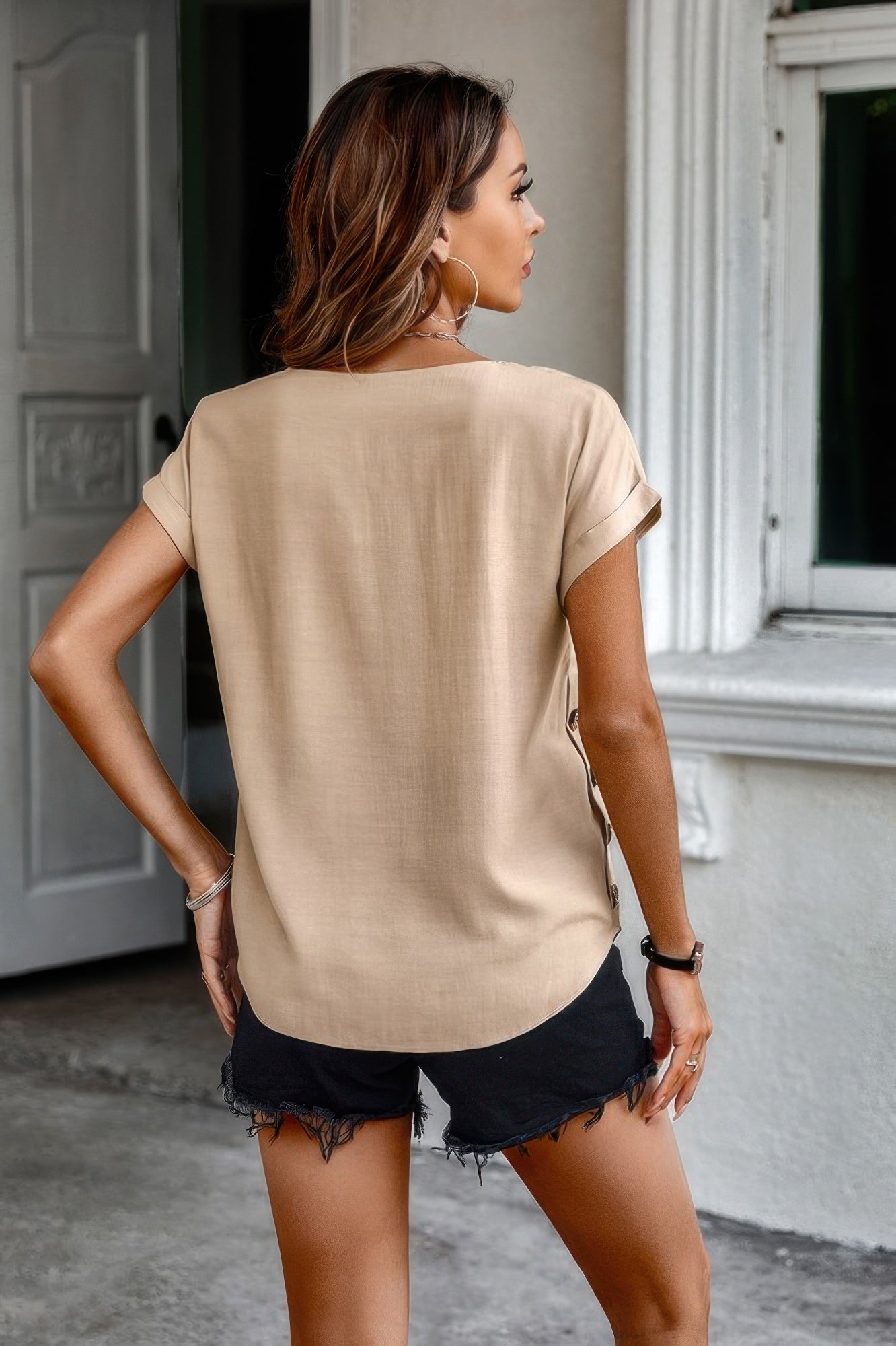 Back view of model wearing beige Batwing Sleeve Blouse with cuffed short sleeves and black frayed shorts
