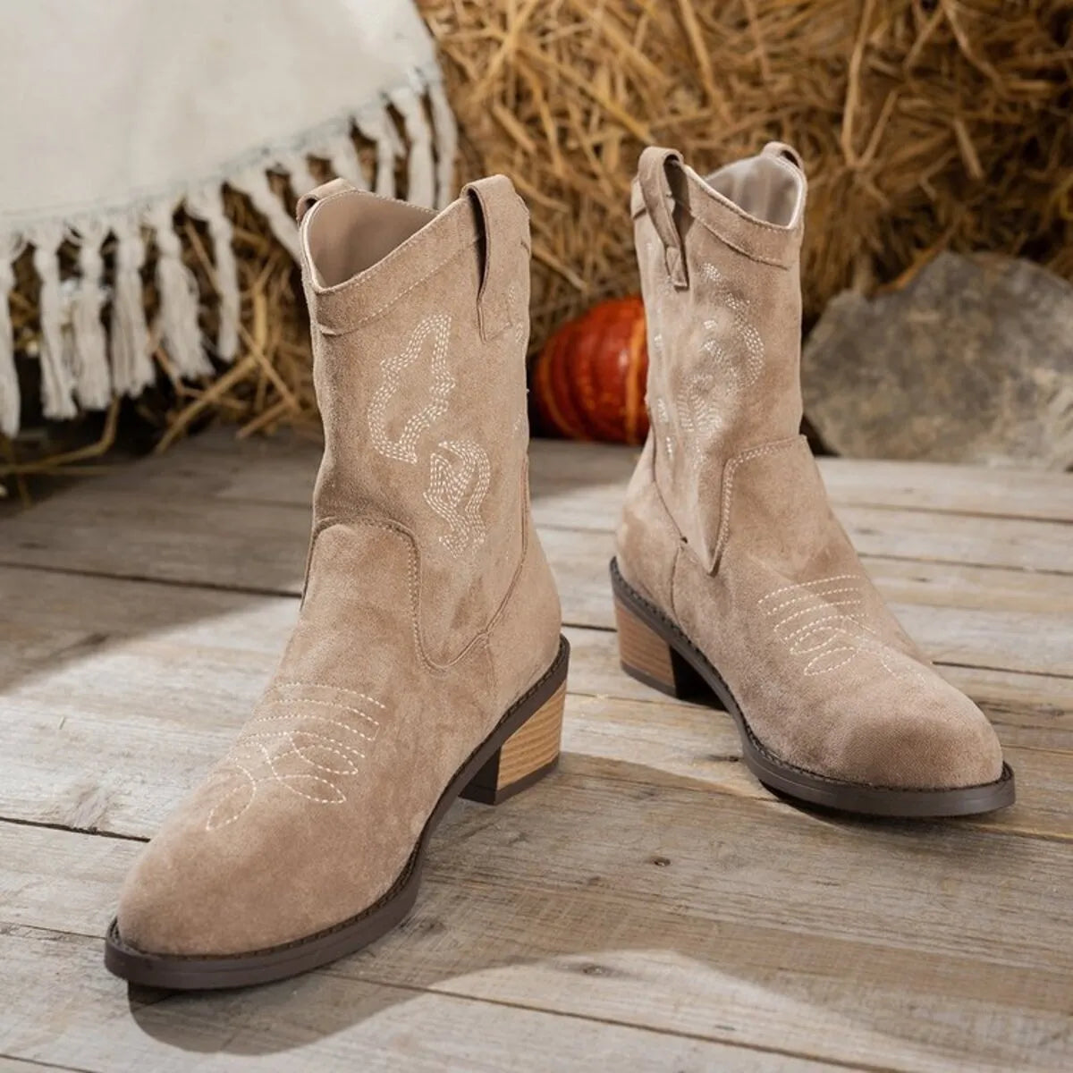 Trendsi beige suede cowboy boots with decorative stitching and stacked wooden heel on wooden floor