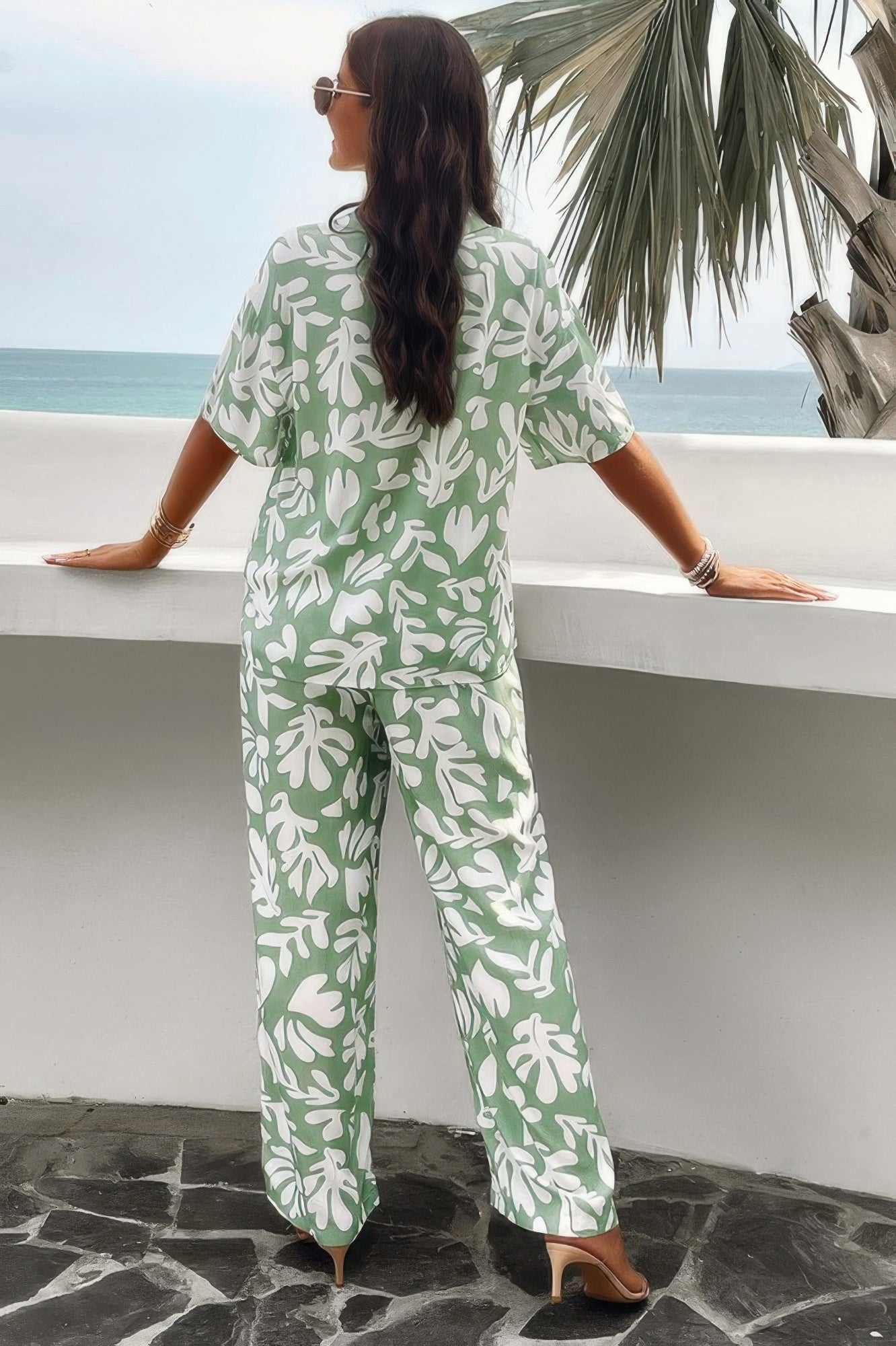 Woman wearing CCWHOLESALECLOTHING green leaf print front button blouse set back view with wide leg pants standing by ocean