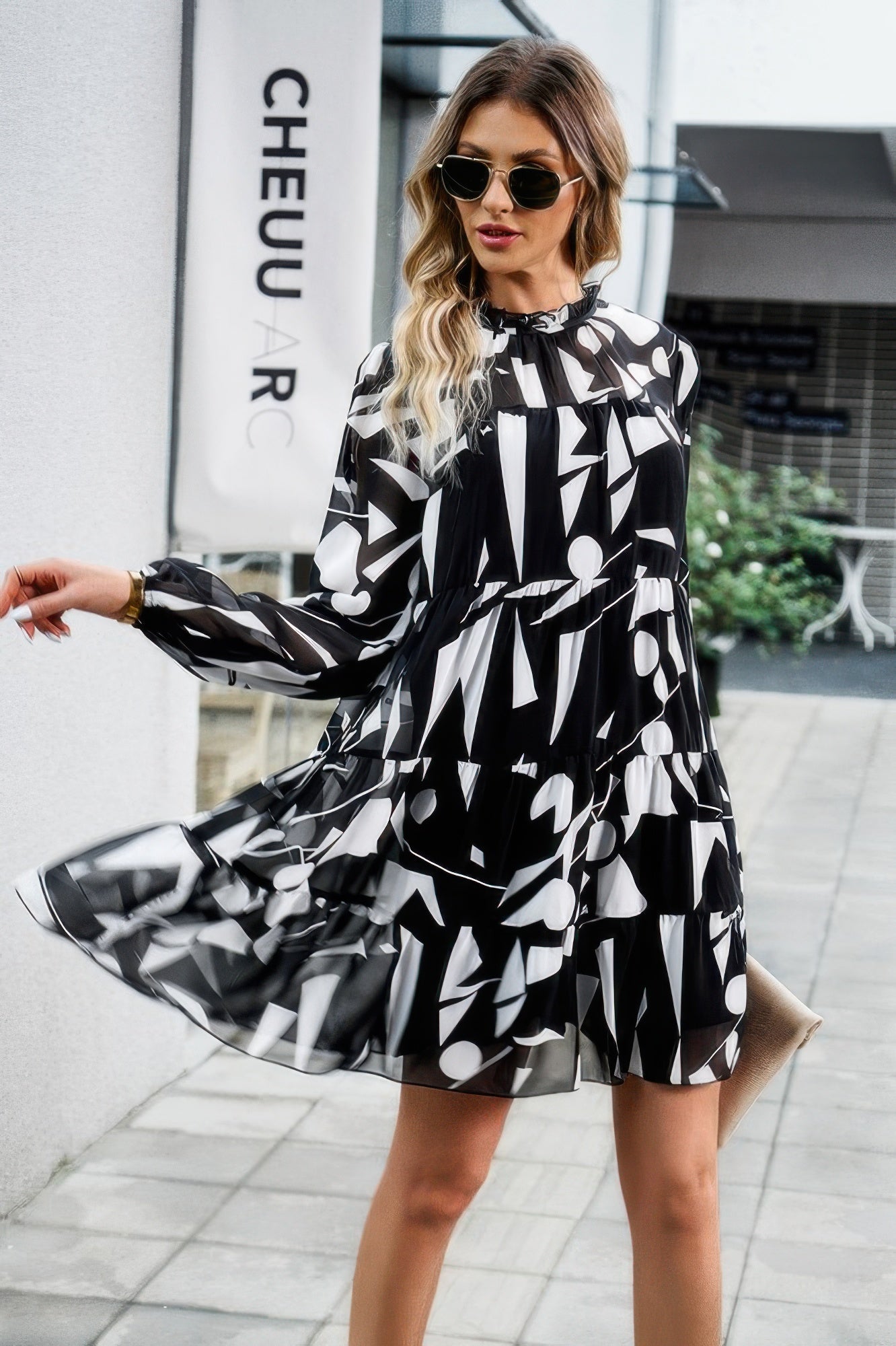 Woman wearing black and white abstract print tiered dress with long sleeves and sunglasses walking outdoors