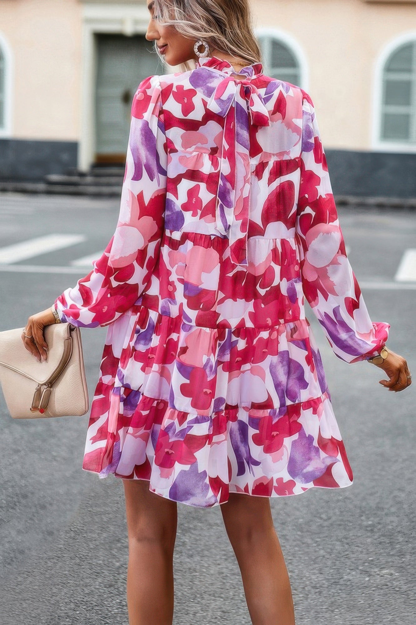 Woman wearing abstract print tiered dress with pink purple red floral pattern and long sleeves and back tie