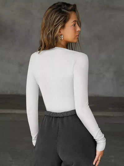 Person wearing a white long-sleeve top and dark pants against a gray background