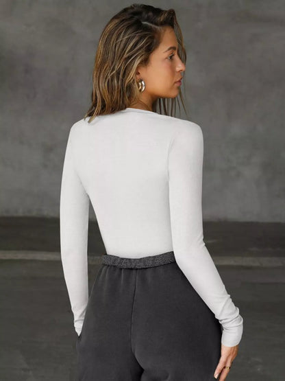 Person wearing a white long-sleeve top and dark pants against a gray background