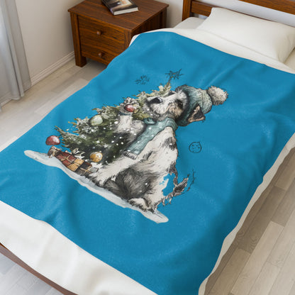 Blue blanket with a winter-themed design of a dog and tree on a bed.