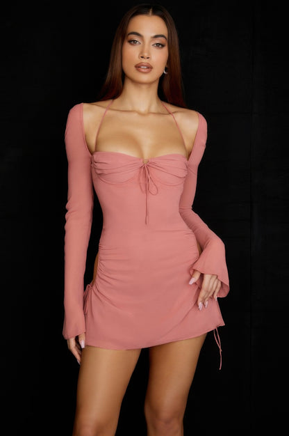 Woman wearing a pink dress with long sleeves against a black background