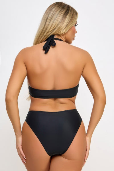 Back view of model wearing cut out black one piece swimsuit with halter tie and high cut leg
