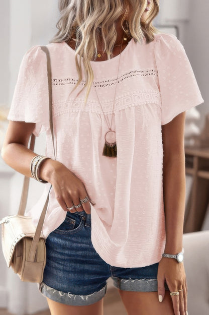 Woman wearing a plus size solid short sleeve top in light pink with lace yoke and textured dots paired with denim shorts
