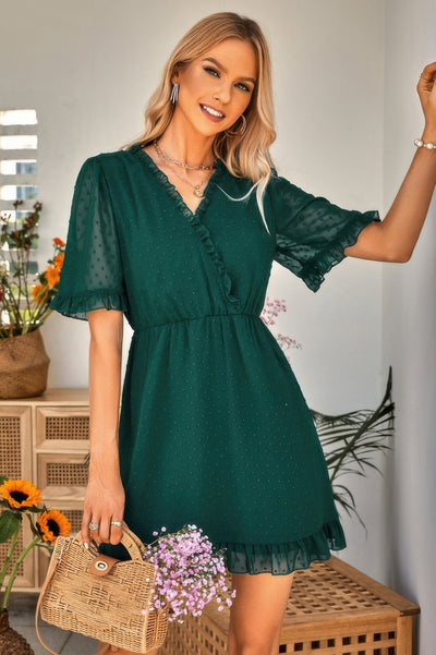 Woman wearing emerald green swiss dot ruffle midi dress with V neck flutter sleeves ruffle hem and wicker bag