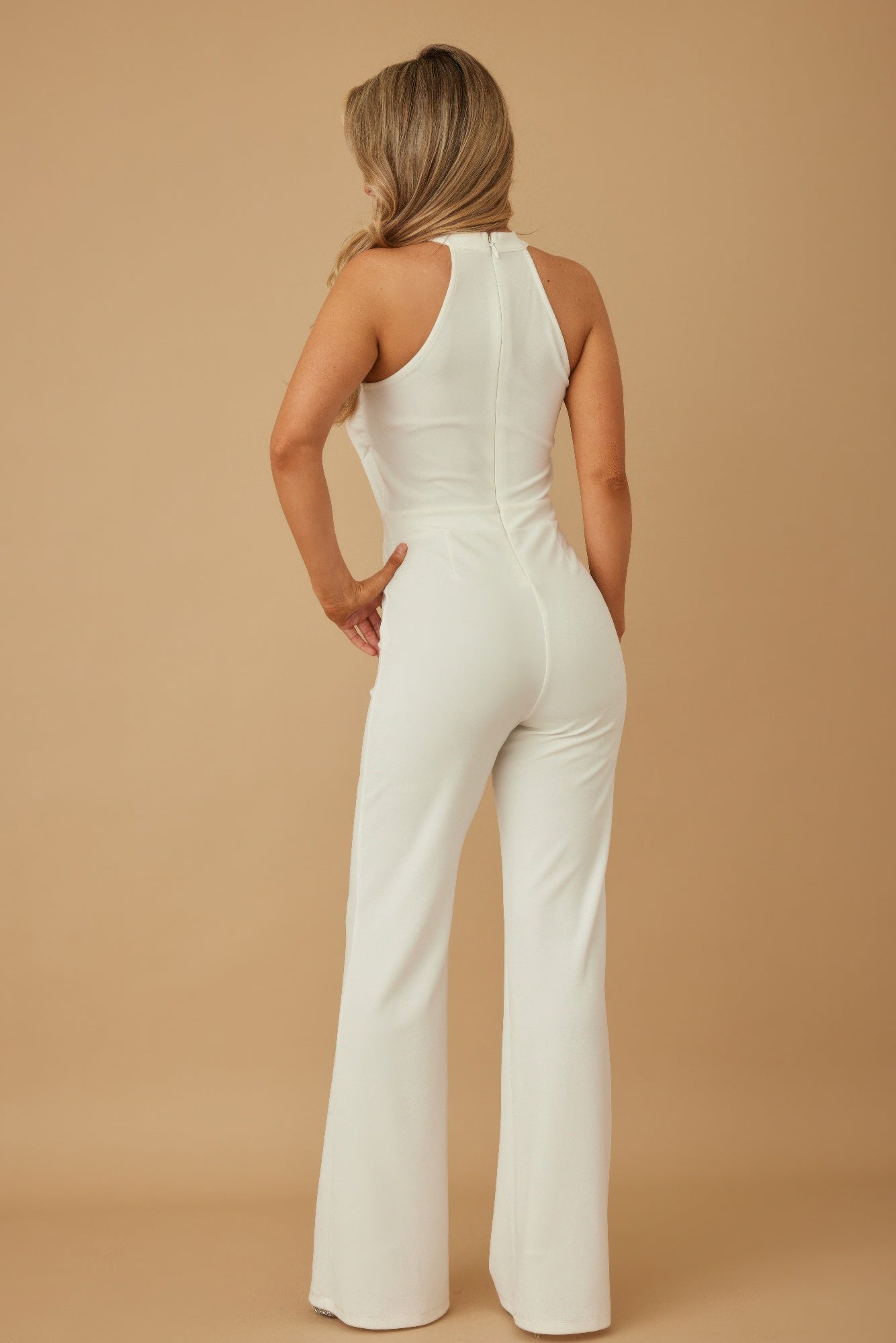 Back view of model in white halter chain jumpsuit by CCWHOLESALECLOTHING with fitted waist and wide legs