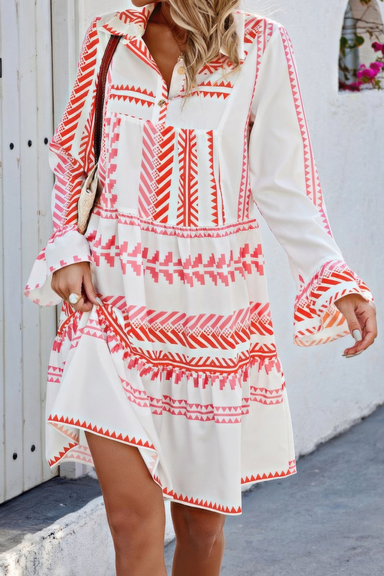 Woman wearing a white and coral geometric print bell sleeve dress with v neck collar and tiered hem
