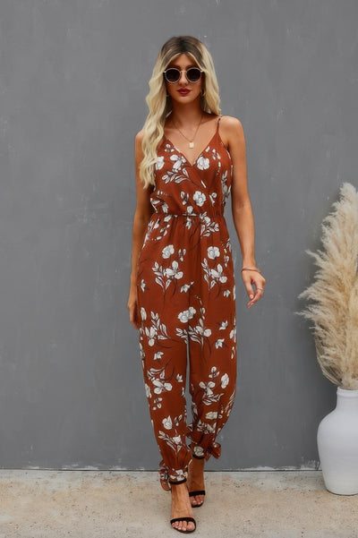 Model wearing rust brown floral print cami jumpsuit with spaghetti straps belted waist ankle ties and sunglasses