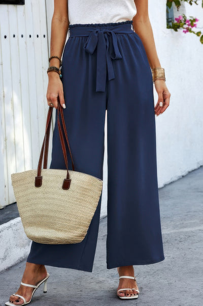 Model wearing navy wide leg high waist Tie Pockets Knot Pants with tie belt side pockets styled with straw tote