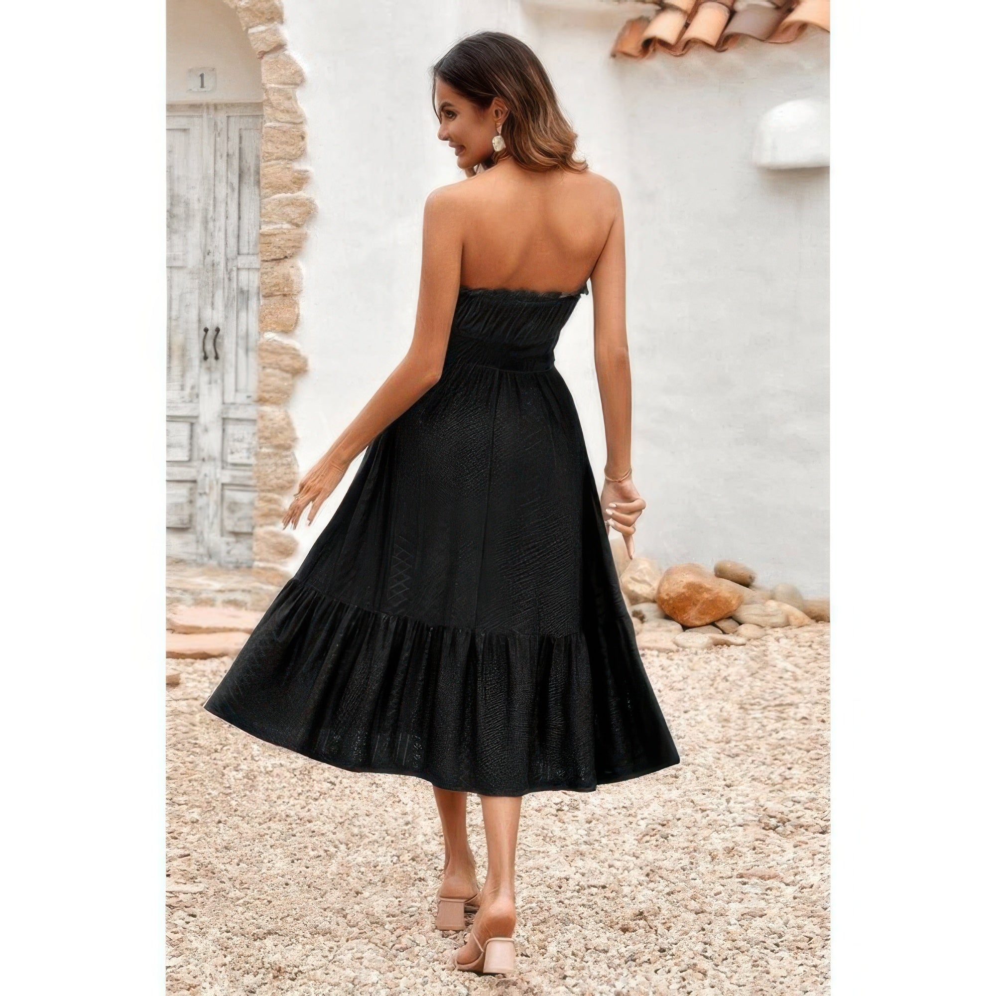Back view of woman wearing Elasit Waist Ruffle Dress black strapless midi dress with ruffle hem and sandals in courtyard