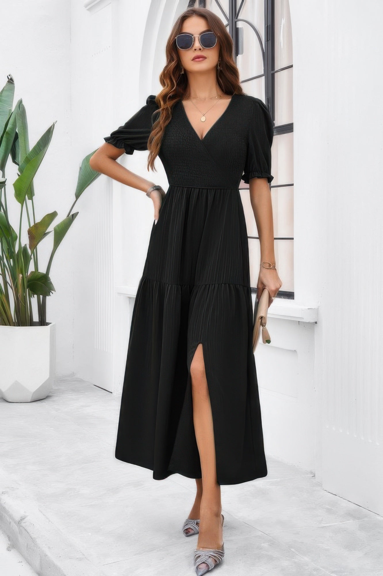 Woman wearing a black High Waist Puff Sleeve Dress with V neck front slit and tiered skirt holding clutch