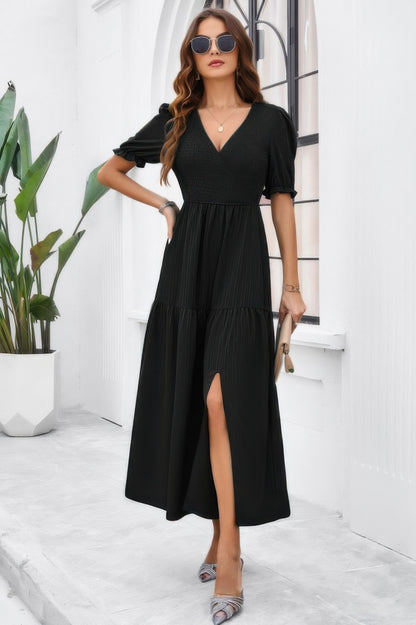 Woman wearing a black High Waist Puff Sleeve Dress with V neck front slit and tiered skirt holding clutch