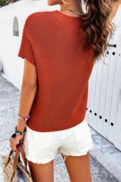 Back view of woman wearing rust ribbed knit loose top with white frayed denim shorts holding straw tote bag