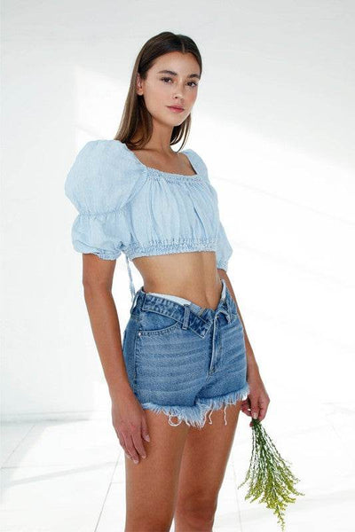 Model wearing Front Ribbon Open Shorts with a cropped blue top in a bright, airy setting