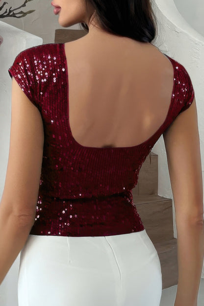 Back view of woman wearing burgundy sequin crop top with scoop back and cap sleeves paired with white pants