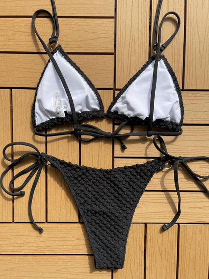Black knit textured bikini summer swimwear with adjustable ties laid flat on wooden surface
