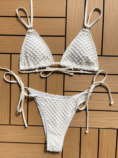 White knit textured bikini summer swimwear with adjustable straps laid flat on wooden surface