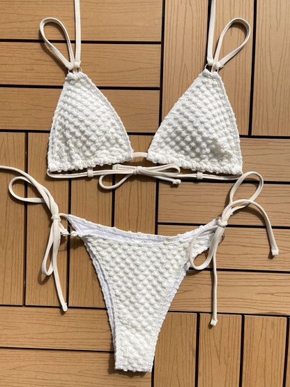 White knit textured bikini summer swimwear with adjustable straps laid flat on wooden surface