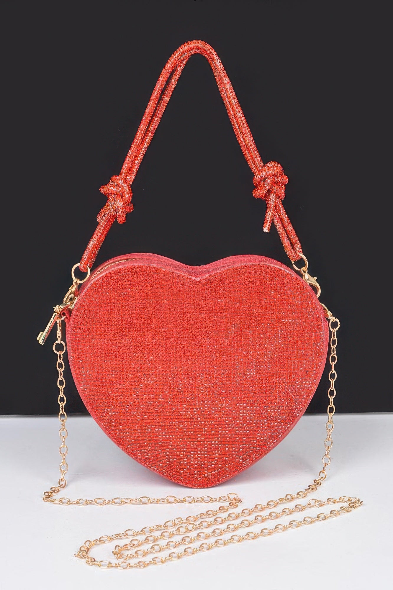 Red glitter Heart Shape Clutch with knotted top handle and detachable gold chain strap on black background