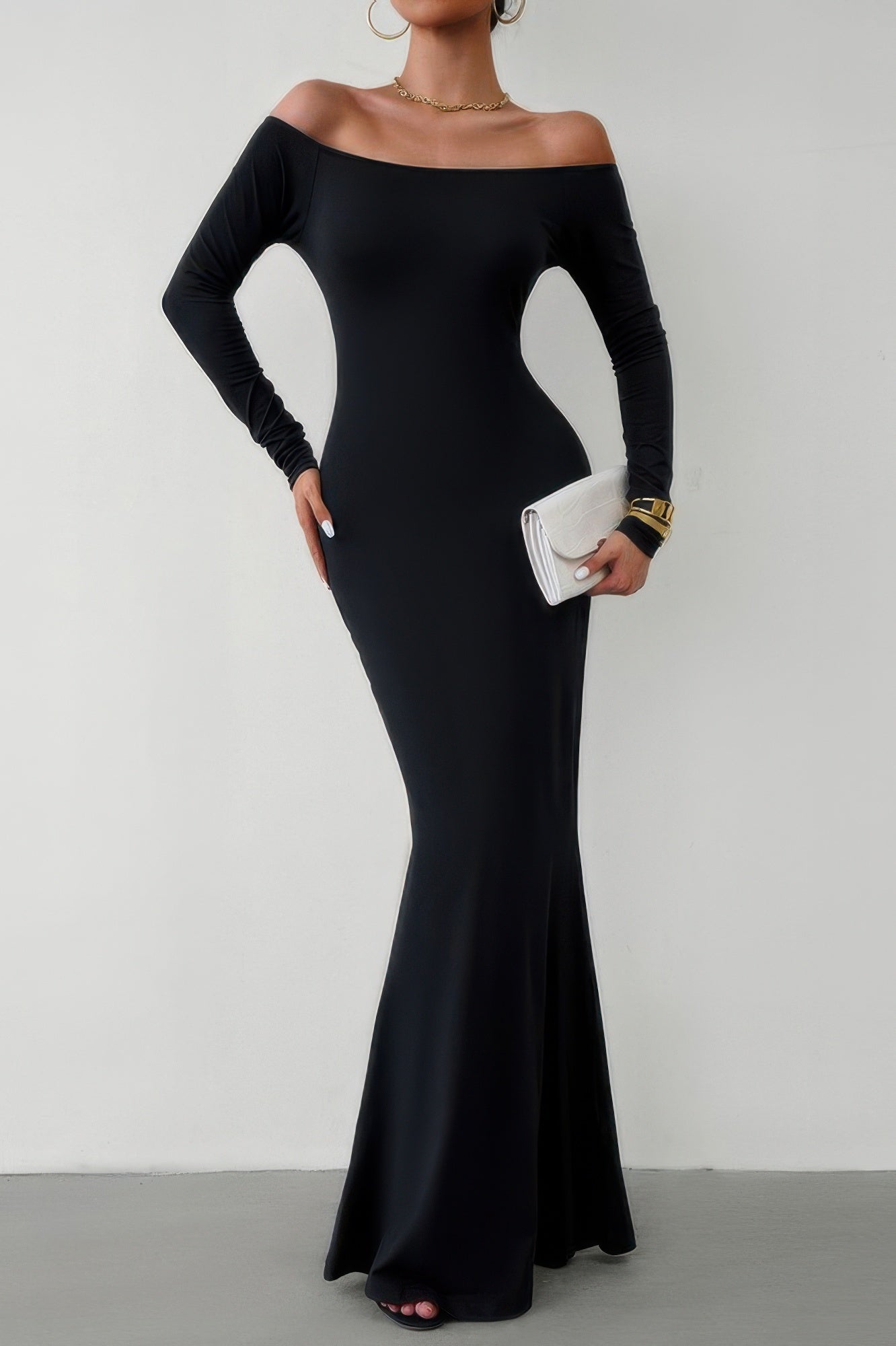Model in black off shoulder bodycon dress long sleeve mermaid hem holding white clutch and gold jewelry