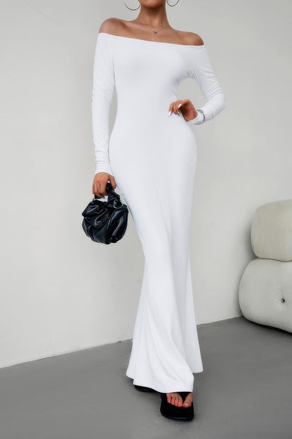 Model wearing white long sleeve off shoulder bodycon dress floor length with black clutch and sandals