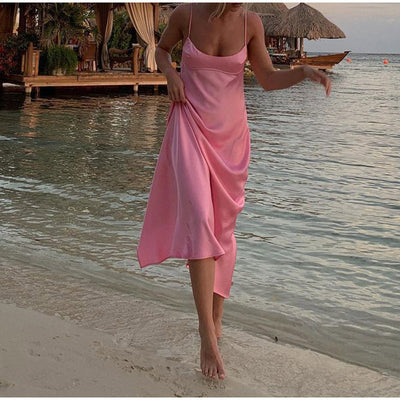 Trendsi pink satin slip dress worn by woman walking barefoot on beach near water