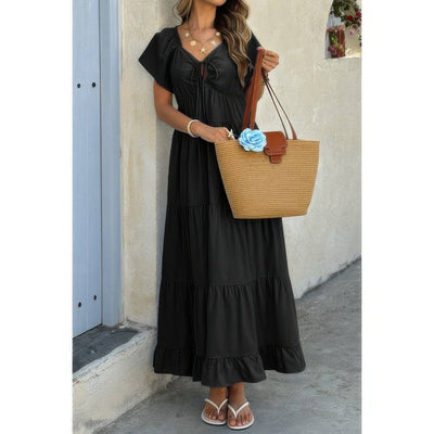 Woman wearing black square neck ruffle hem dress with tiered skirt and straw tote bag