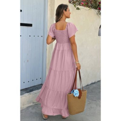 Woman in mauve maxi square neck ruffle hem dress with smocked bodice and puff sleeves carrying straw tote